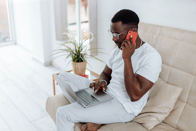 A man at home speaking on his phone and working on his laptop