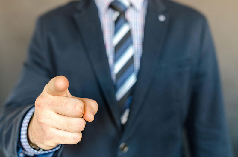 Closeup of a man in a suit pointing his finger at the camera