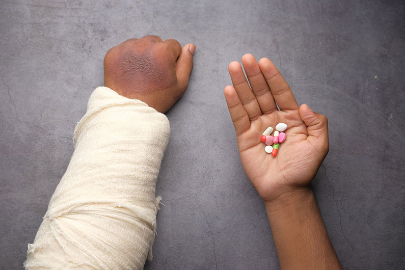 One injured hand is wrapped in a bandage and the other has pills in the palm