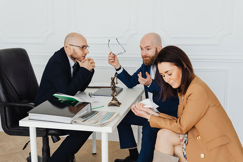 A man and a woman appear to be in the midst of a legal arbitration or mediation conducted by a man at a desk.