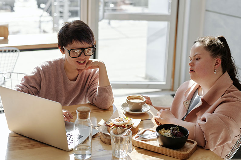 A woman with a disabling condition and another person look at a laptop