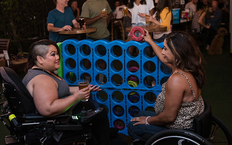 Two women in wheelchairs play a game in a bar
