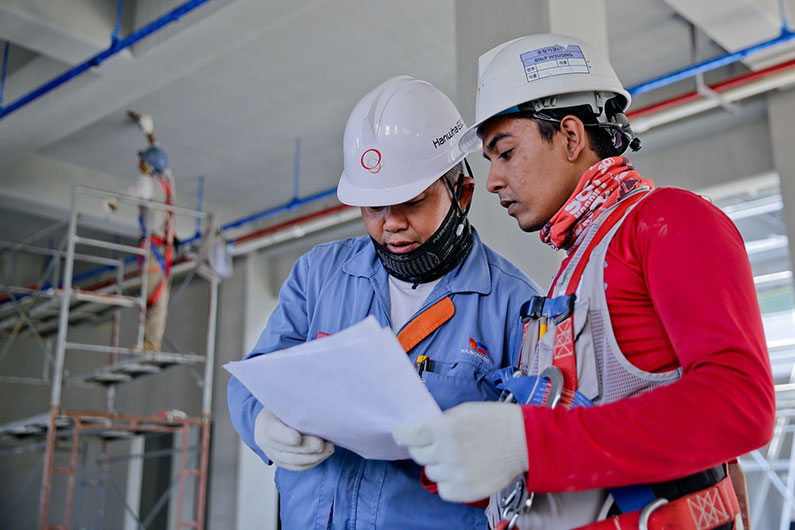 Two employees in safety gear look at a paper