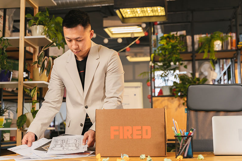 A terminated employee puts items into a box on his desk labelled "Fired."