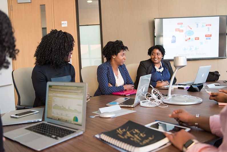 Professional women of colour sit at a table in a conference room.